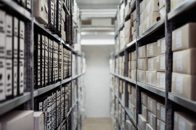 A narrow aisle between shelves filled with organized boxes and files.