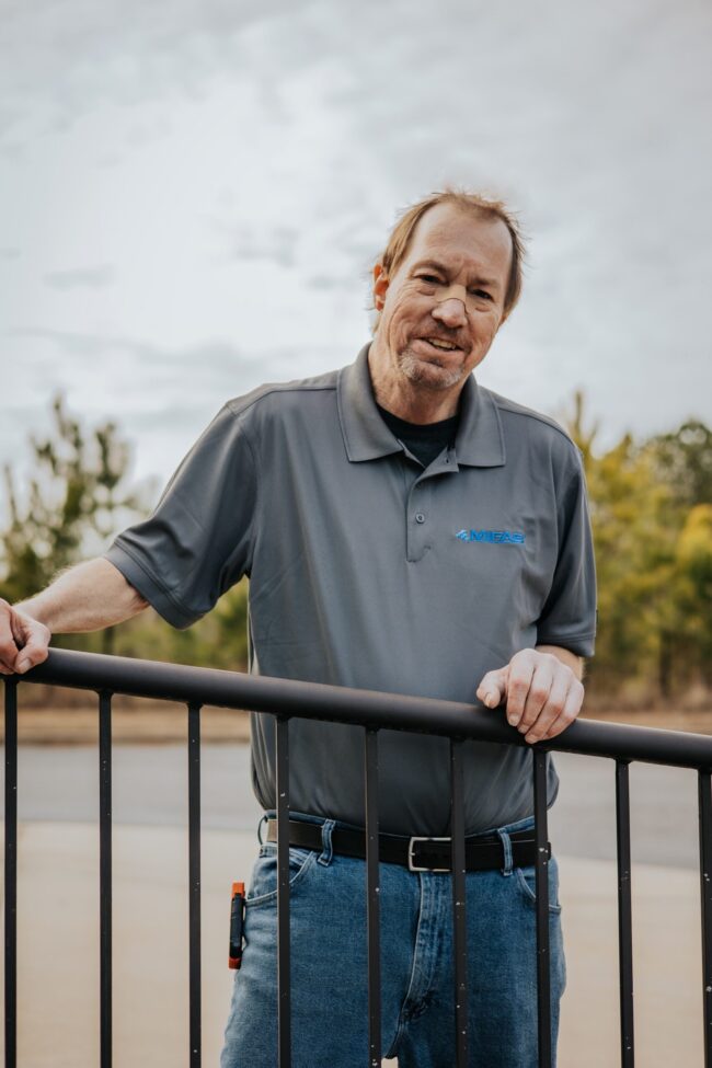 Man in a gray polo shirt leaning on a railing outdoors.