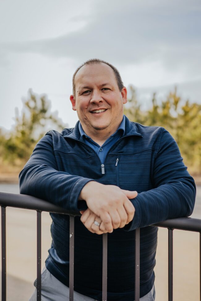 Smiling man leaning on a railing outdoors.