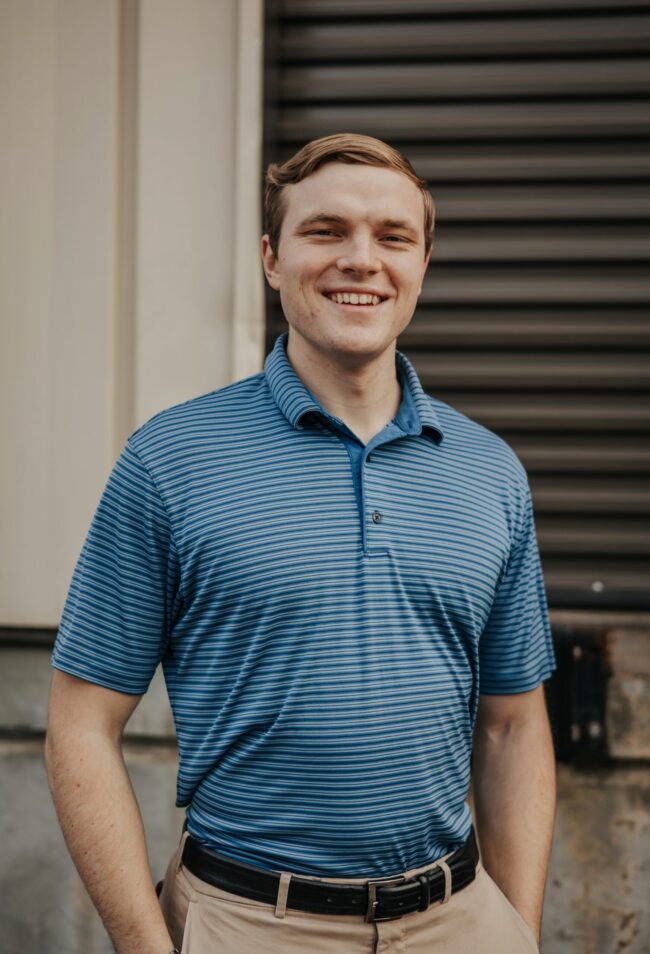 Smiling young man in a blue striped polo shirt poses outdoors.